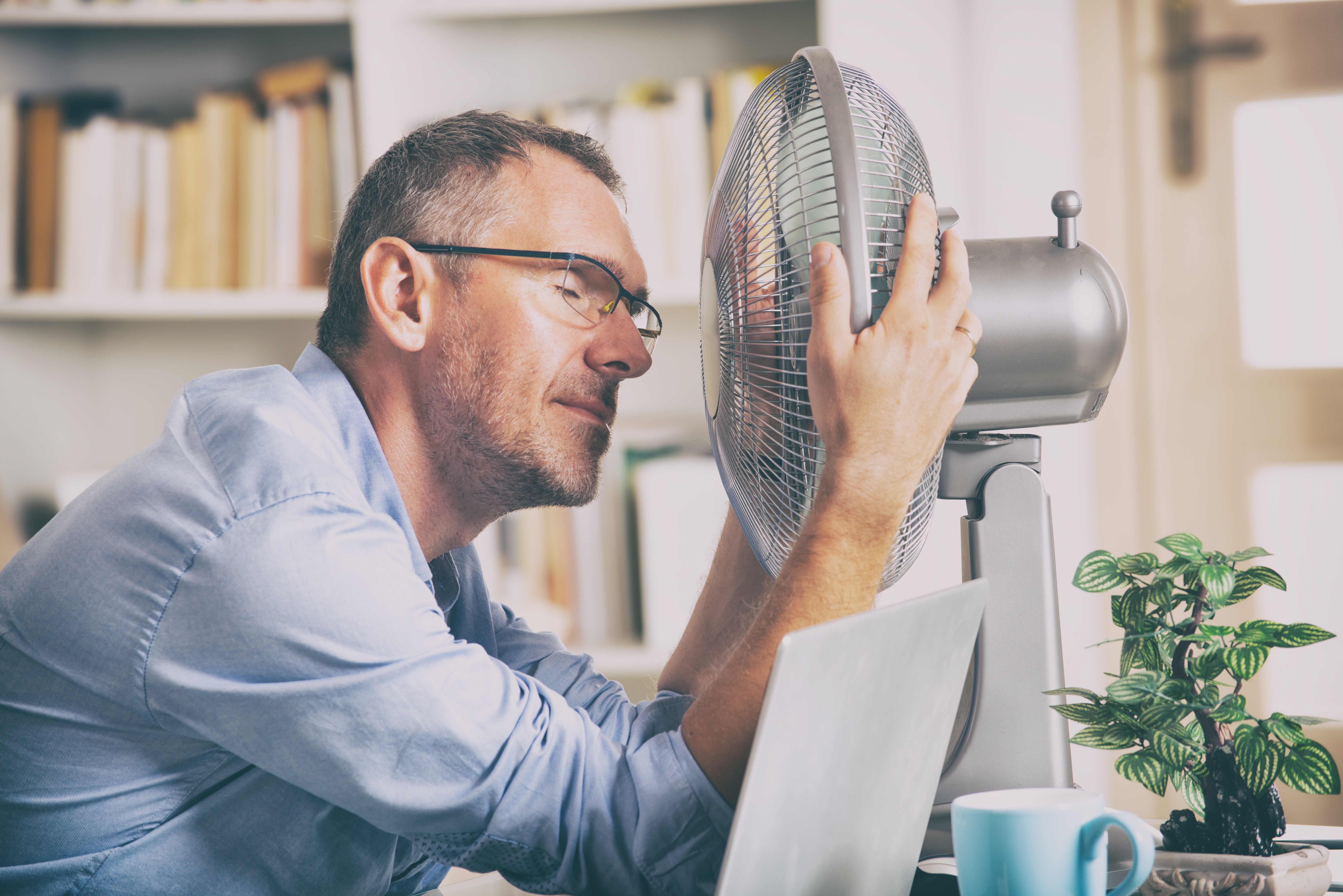 man tries to stay cool with a fan in his home office